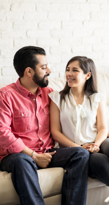 Two people sitting on a couch in front of a white brick wall